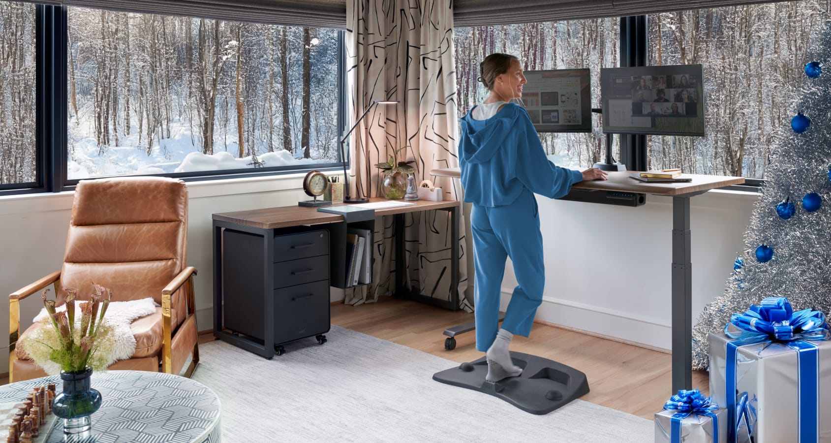 women standing at an electric standing desk raised in a home office with a christmas tree in the corner of the room